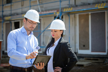 Two architects a man and a woman in construction in white helmets.