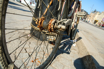 A detail picture of the old unused abandoned bicycle left behind on the street. The chain is rusty and worn away. 