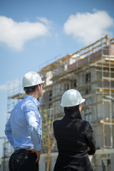 Two architects a man and a woman in construction in white helmets.