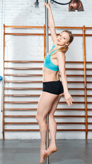 Fototapeta na wymiar Young slim athletic woman dancing strip plastic on pylon in fitness class