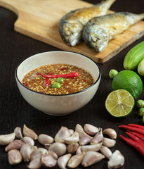 Chili paste (thai language Nam prik kapi) in a white bowl with ingredients and Fried steam mackerel on the table.