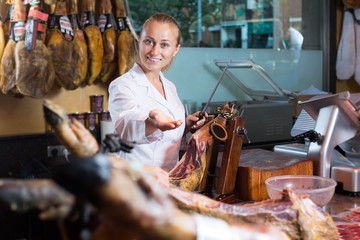 Woman seller working with iberian jamon in meat shop