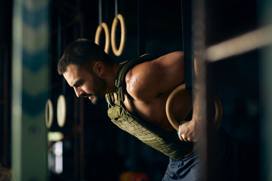Shirtless man exercising on gymnastic rings in gym