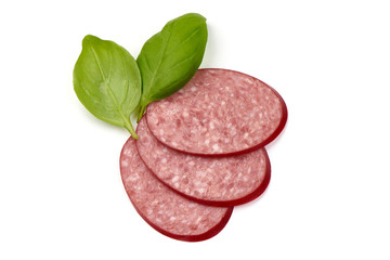 Sliced dry salami sausage with basil leaves, close-up, isolated on white background