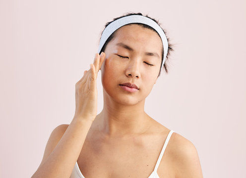 Young natural asian woman portrait applying moisturiser.
