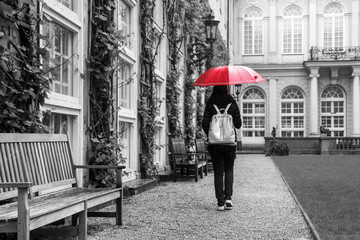 The woman with the red umbrella is walking in the historical garden of a castle during the rainy day. 