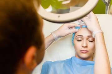 Naklejka premium Woman makes botox injections in forehead area. Doctor cleans the girl's face from wrinkles. Plastic surgery in private medical clinic.