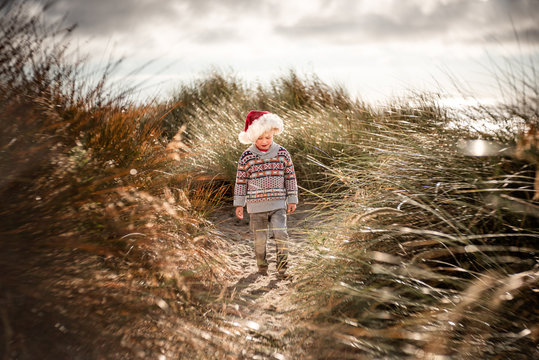 Toddler boy wearing Santa hat walking in sand dunes in the morning