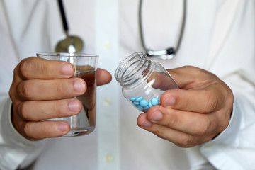 Doctor holding bottle of pills and glass of water, therapist giving medication in blue tablets. Concept of medical exam, prescription, dose of drugs, vitamins, pharmacy