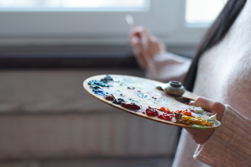 Close-up of female hands mixing paints on a palette with a spatula creating an oil painting