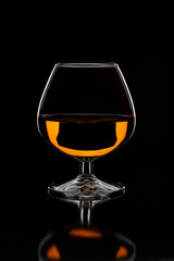 Brandy glass filled with half alcoholic drink on a black background in a beautiful light.