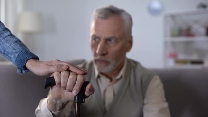 Female hand comforting old man leaning on stick, hospice care for disabled