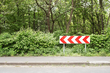 Eine Richtungstafel linksweisend vor grünen Büschen und Bäumen