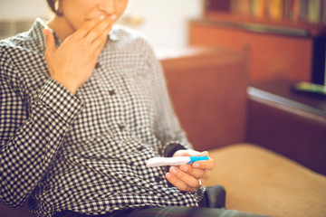 Finally pregnant. Attractive young women looking at pregnancy test and smiling while sitting on the sofa at home