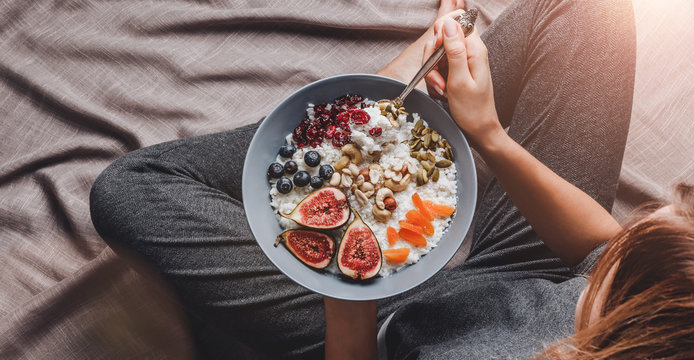 Woman in home clothes eating vegan Rice coconut porridge with figs, berries, nuts. Healthy breakfast ingredients. Clean eating, vegan food concept.