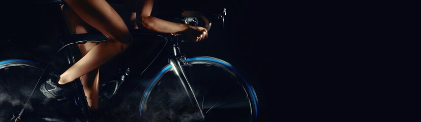 Cropped image bicycle wheels motion digital art effect body part slim legs of woman riding on bicycle aside, studio shot horizontal photo on black background with copy free pace for advertisement text