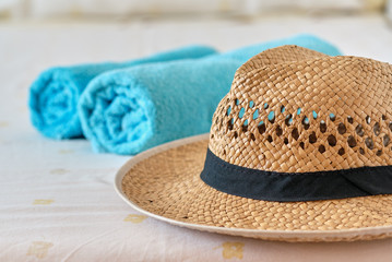 Beach holidays accessories close up. Woman straw hat on foreground, folded two blue color towels lie on bed, no people. Concept image of summer season vacation