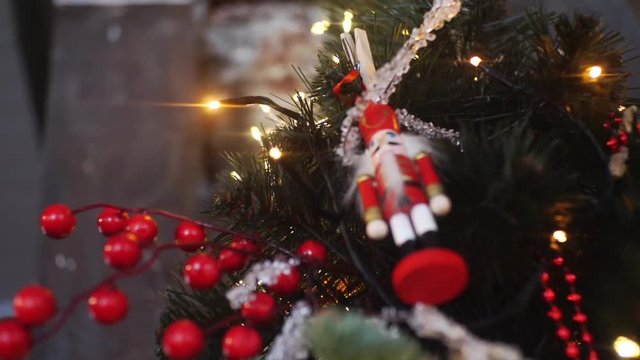 View from the bottom of traditional nutcrackers figurine in red suit hanging on a Christmas Tree near the lights and other decorations. Frame. Christmas mood