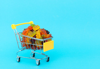 sweet and tasty pastry - marmalade bears, jelly candies, in the food basket, shopping trolley on a blue background with space for text. horizontal frame