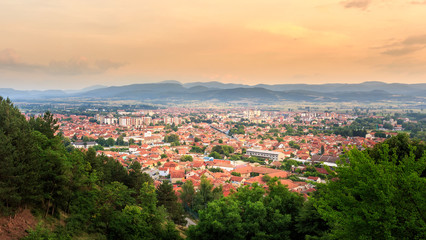 Golden hour sky over sunlit Pirot city in Serbia and green foreground trees