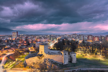 Naklejka premium Blue hour Pirot cityscape with ancient 14th century fortress Momcilov grad in the foreground, purple sky and city lights