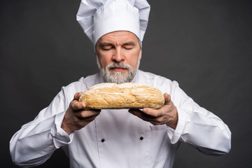 Portrait of a male chef cook smelling fresh bread against black background.
