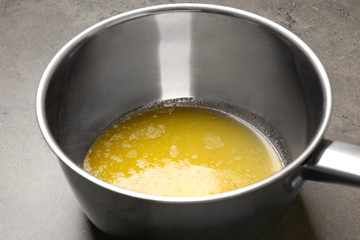 Saucepan with melting butter on grey table, closeup