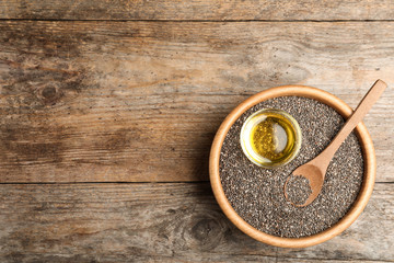 Bowl with chia seeds, oil and spoon on wooden table, top view. Space for text