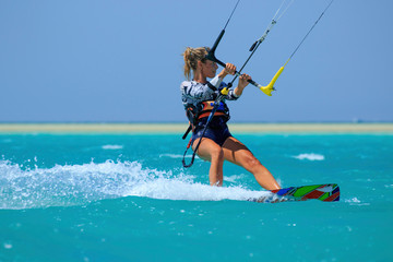 Kite surfing girl in sexy swimsuit with kite in sky on board in blue sea riding waves with water splash. Recreational activity, water sports, action, hobby and fun in summer time. Kiteboarding sport - obrazy, fototapety, plakaty