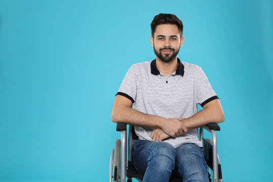 Young Man In Wheelchair On Color Background. Space For Text