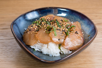 bowl with salmon sashimi seasoned with black and white sesame, rocket, nori seaweed fried on a bed of steamed white rice