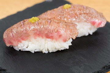 nigiri of heat-burned kobe beef dressed with mustard, served on a square plate of slate