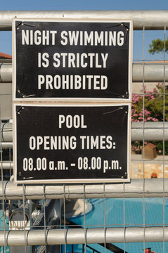 Sign by a European holiday swimming pool warning that swimming during the night is strictly prohibited.