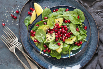 Healthy vegetarian avocado salad  with spinach, pomegranate and sesame in the plate on dark background. Top view with copy space.