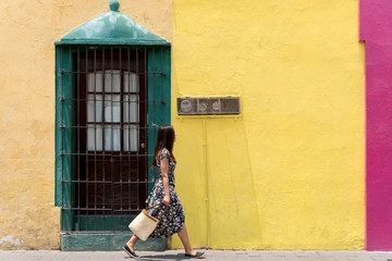 Woman wearing a dress and a bag walking in front of a colorful facade in Cholula, Mexico