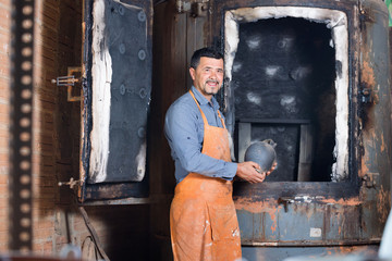 Cheerful craftsman carrying fresh baked black glazed vessel