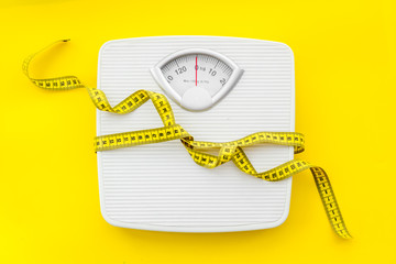 bathroom scales and measuring tape for weight loss concept on yellow background top view