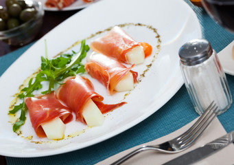 Rolls of iberian jamon stuffed with melon at plate with arugula
