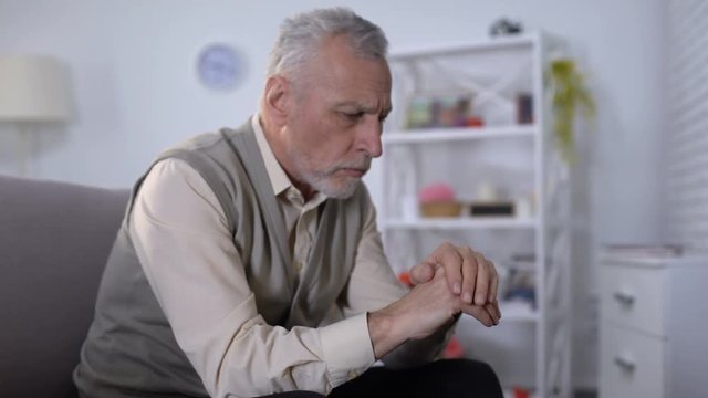 Old man looking at hand trembling, distressed by tremor, early Alzheimer symptom