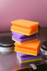 Obraz na płótnie Canvas A stack of purple and orange sponges for washing on the stove. The concept of housework and cleaning. Several sponges on the hob.