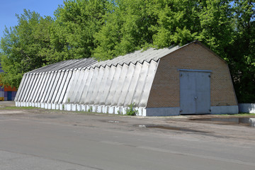 Fototapeta premium Industrial hangar with aluminum walls and roof stands on a concrete foundation near green trees