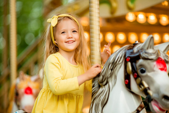 Adorable little girl near the carousel outdoors in Paris, baby girl on the carousel, Happy healthy baby child having fun outdoors on sunny day. Family weekend or vacations