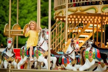Fototapeta na wymiar Adorable little girl near the carousel outdoors in Paris, baby girl on the carousel, Happy healthy baby child having fun outdoors on sunny day. Family weekend or vacations