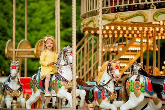 Adorable little girl near the carousel outdoors in Paris, baby girl on the carousel, Happy healthy baby child having fun outdoors on sunny day. Family weekend or vacations