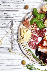 antipasto various appetizer. Cutting board with prosciutto, salami, cheese, bread and olives on white wooden background
