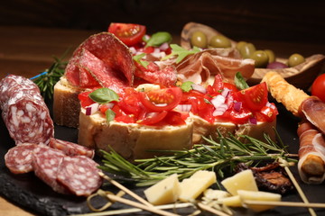 Traditional italian antipasto bruschetta appetizer with cherry tomatoes, cream cheese, basil leaves and balsamic vinegar on cutting board with prosciutto, salami, cheese
