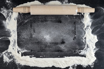 wooden rolling pin on a black background, scattered white wheat flour