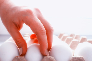 the hand takes the egg from the tray, as the concept of the buyer’s demand for chicken eggs as...