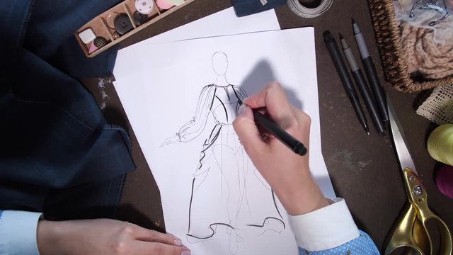 Timelapse of sketch drawing, top view of female skillful hands holding felt pen and creating dress sketch. Professional seamstress and designer making sketch at worktable in atelier