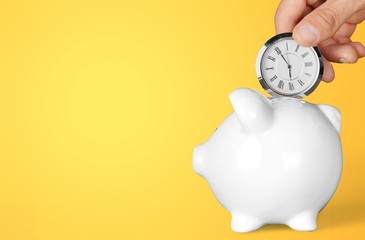 Hand depositing  clock  in piggy bank on background
